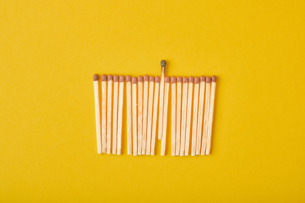 A set of matches laid out on a yellow background. One burnt of the manages is burnt.