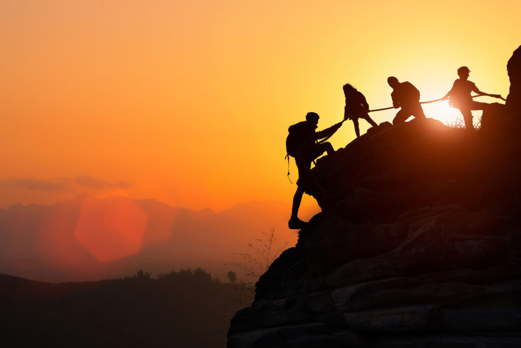 Silhouette of a team climbing up a mountain together. The concept of resilience.